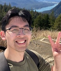 Man wearing a green shirt holding a peace sign up in front of mountains.