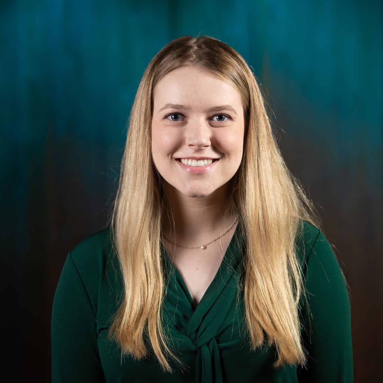 A blonde-haired woman in a green shirt smiles at the camera.