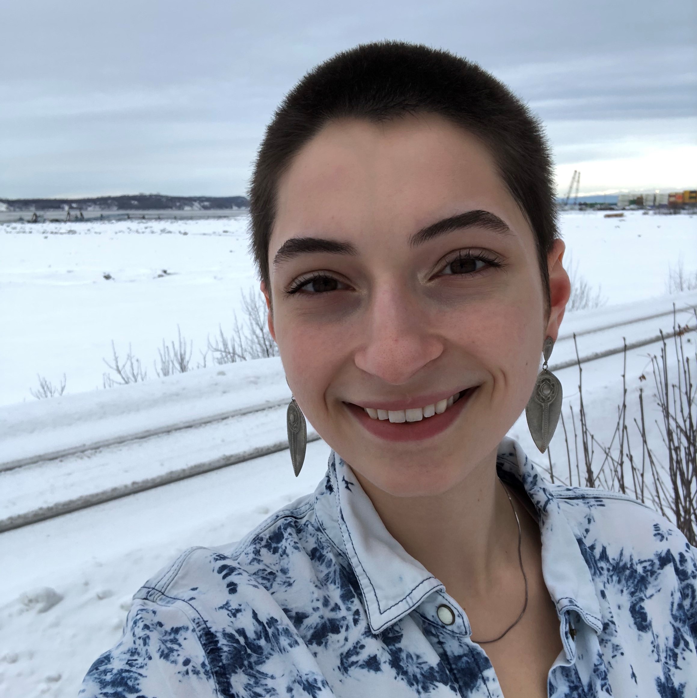 Woman stands in front of a snowbank on a cloudy day.