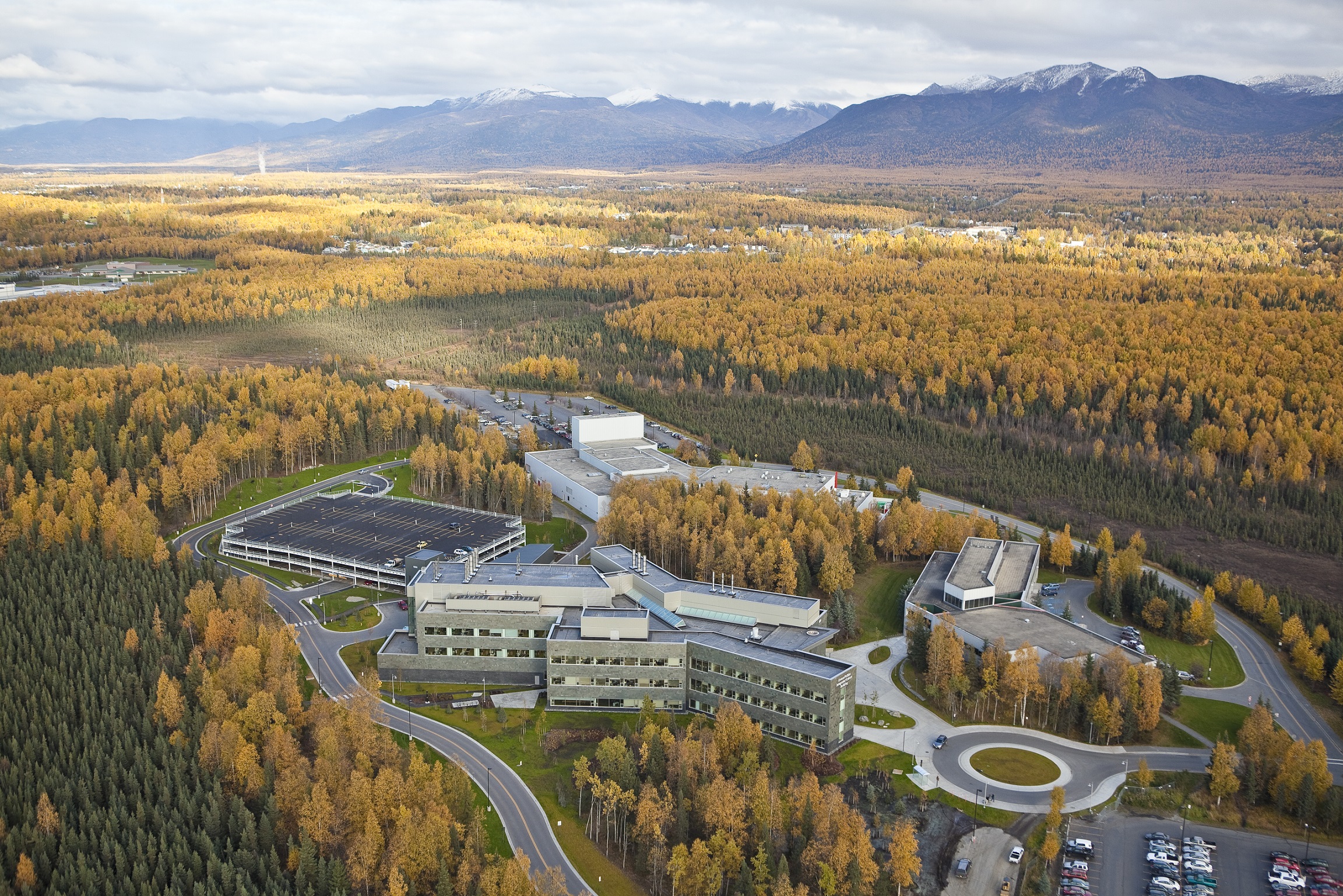 Aerial view of UAA campus with autumn gold trees and snow capped mountains in the background