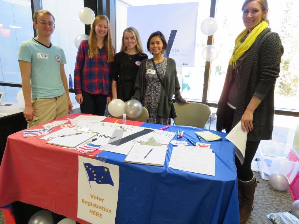 Voter registration table in the Student union with group of students and one faculty member behind the table smiling.