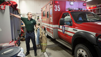 An instructor holding a uniform infront of an ambulance