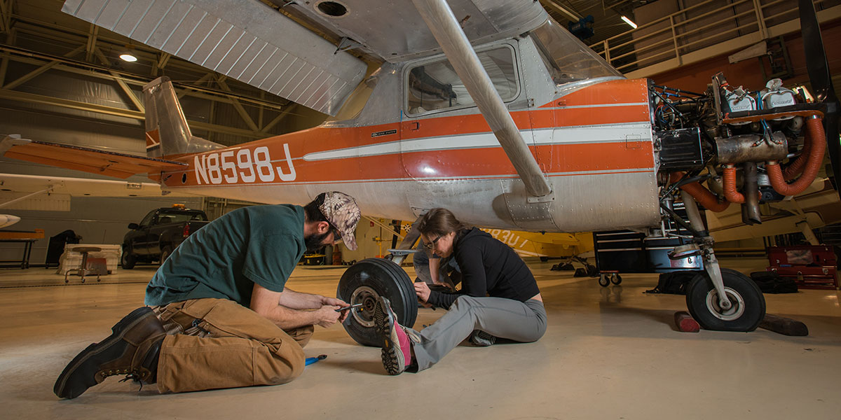 Two students working on the wheel of an orange plane