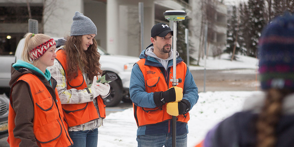 Students in the snow holding surveying equipment and wearing protective gear