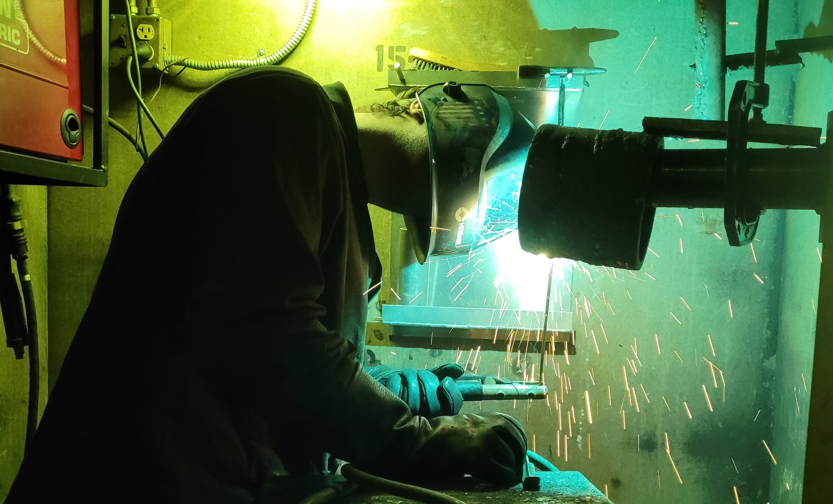 Student welding on pipe in booth