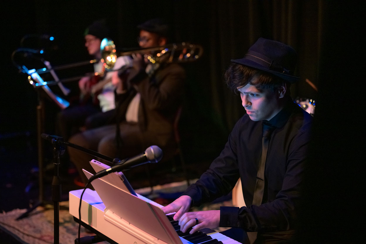 Musician playing keyboard with trombone players behind him
