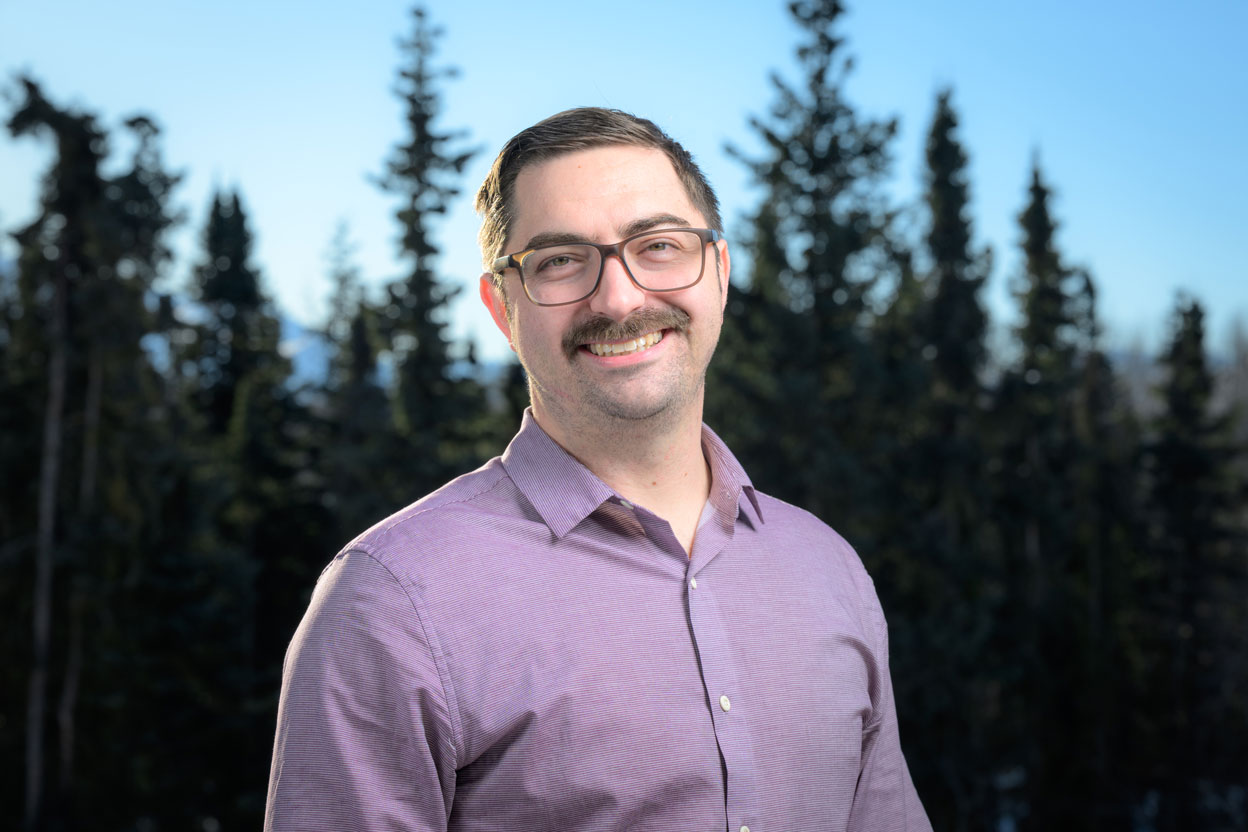 Man wearing lavender shirt in front of trees