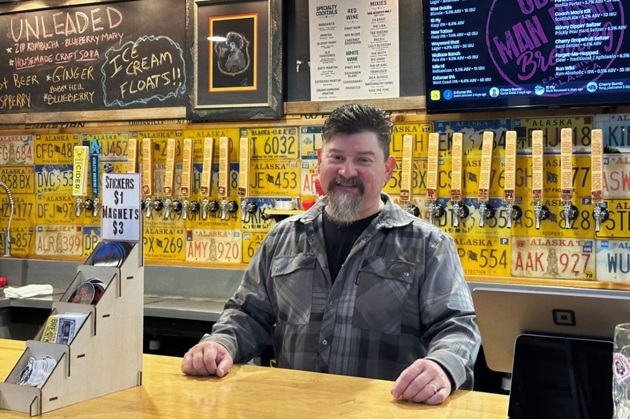 A smiling man stands behind a bar counter, looking ready to serve beer.