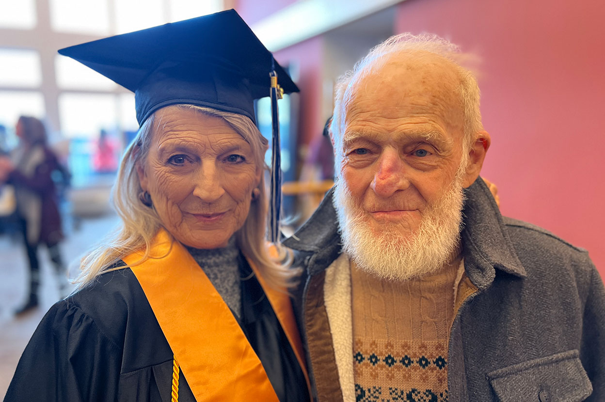 Woman in graduation gown and her husband smiling for the camera