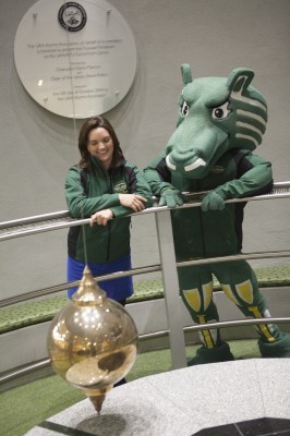 Nona Wilson, Senior Alumni Relations Specialist, and Spirit, professional mascot, take a work break at the UAA Alumni Association's Foucault pendulum. Photo by Philip Hall/University of Alaska Anchorage.