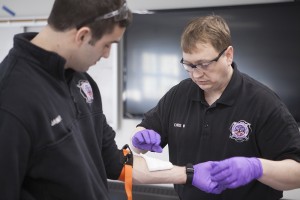Student Chris Wilkins, right, practices putting a tourniquet on James Reinhart, another student, during a paramedic course at Mat-Su College. (Photo by Philip Hall/UAA)