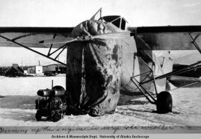 An airplane stands in the snow at a field believed to be Merrill Field, its engine covered with a tarp and a heater aimed at the plane. (Photo from Beulah Marrs Parisi Collection, Special Collections and Archives, UAA/APU Consortium Library)
