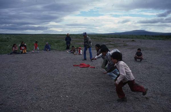 Four boys start a foot race while adults and other children watch, during Fourth of July festivities in Buckland, 1976. UAA/APU Consortium Library Archives and Special Collections, uaa-0165-b11-f1-77