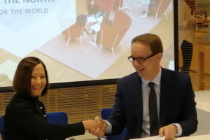 UAA Chancellor Cathy Sandeen sits at a table with Antti Syväjärvi, rector of the University of Lapland in Finland. They are shaking hands after signing a memorandum of understanding. Chancellor Sandeen is looking at the camera and smiling.