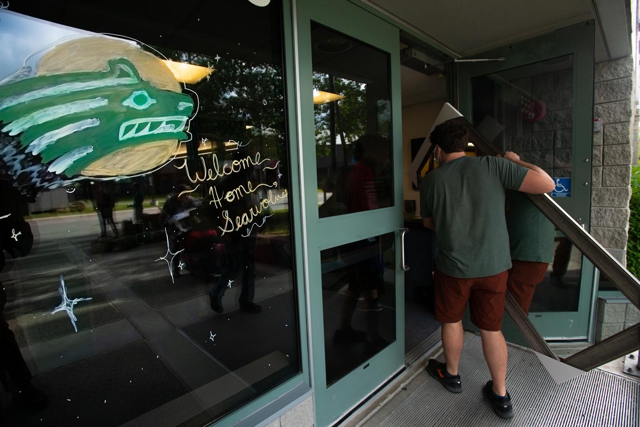 Student carries a mirror into UAA residence hall that features 'Welcome home, Seawolves!' drawing on the entrance door. (Photo by James Evans / UAA)