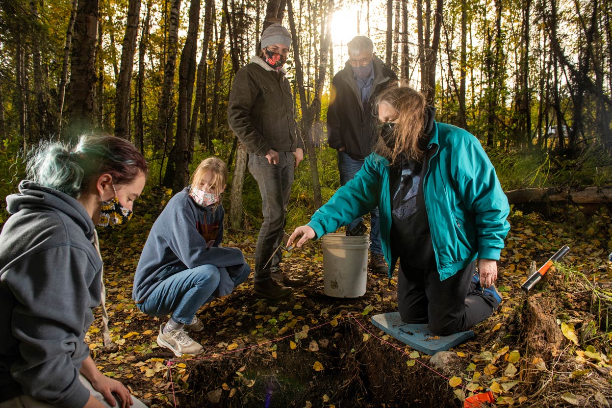 UAA Associate Professor of Anthropology Diane Hanson guides anthropology students as they excavate a bear skeleton that has been buried in the forest near UAA since 2019.