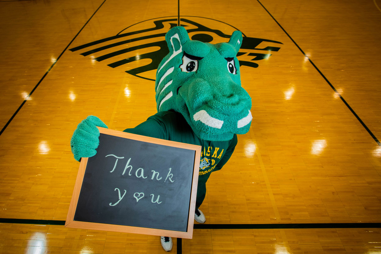 Spirit the Seawolf holds up a chalkbaord with "Thank You" written on it.