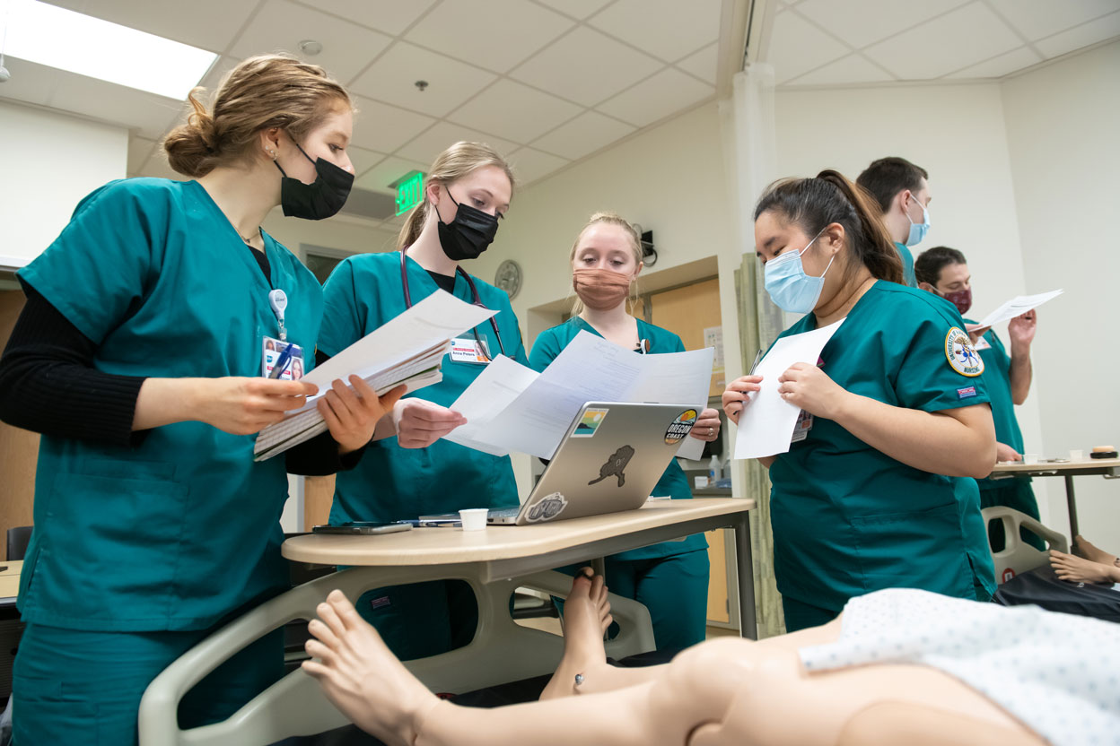 UAA School of Nursing students Clara Moyer, Anna Peters, Katie Warner, and Eunice Kang practice patient assessment, taking vital signs, and giving medication in the nursing skills lab in UAA's Health Sciences Building.