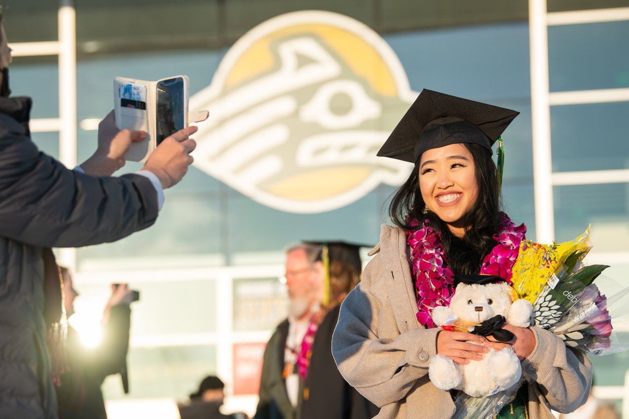 Barbara Yang, BBA Management, has her picture taken outside the Alaska Airlines Center after receiving her degree at UAA's fall 2021 commencement ceremony. (Photo by James Evans / UAA)