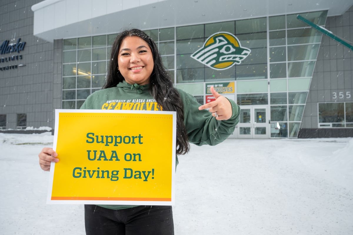 UAA student holding a sign with the words "Support UAA on Giving Day"