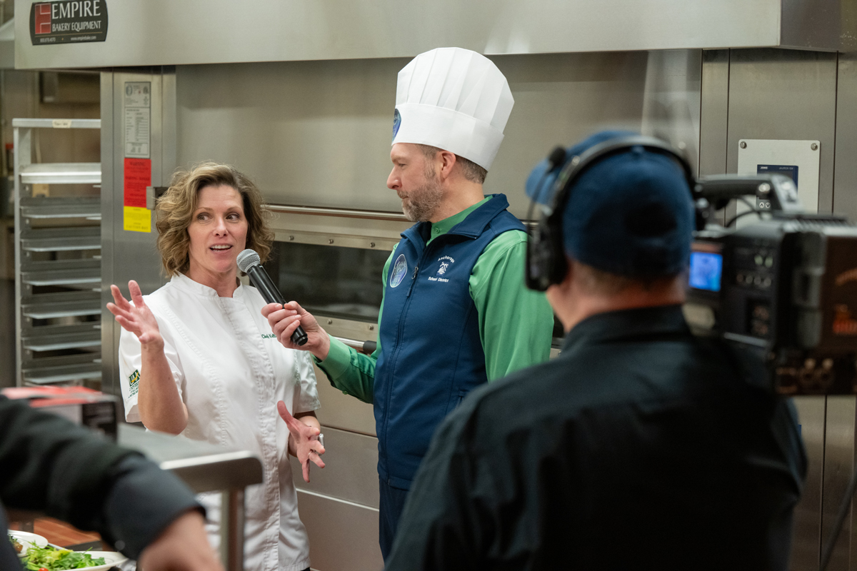 Roving reporter MJ Thim interviews department chair and assistant professor Kellie Puff in the kitchen during UAA's 2024 Celebrity Chef Invitational. 