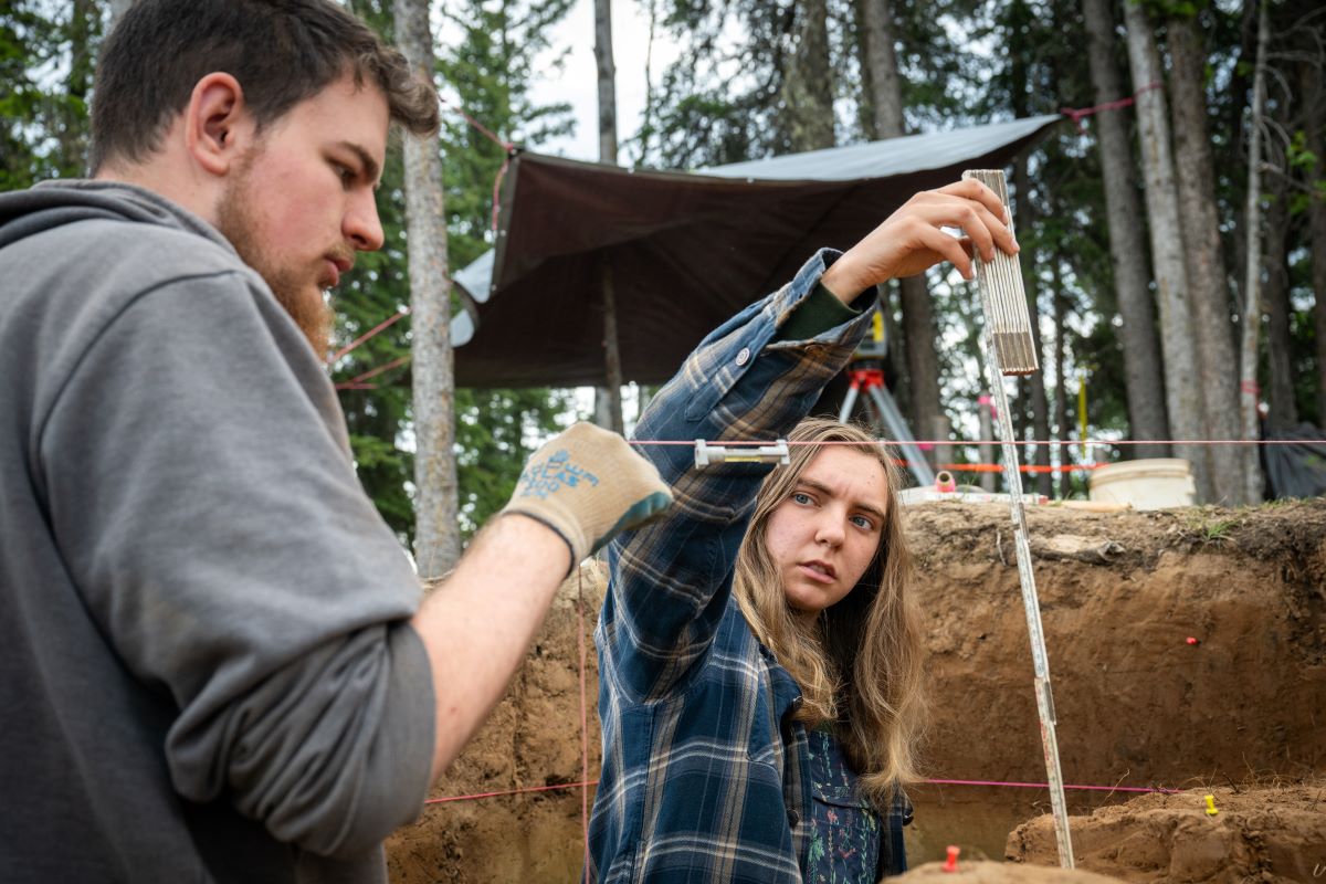 Two archaeologists measure a stratigraphic layer using a level and string
