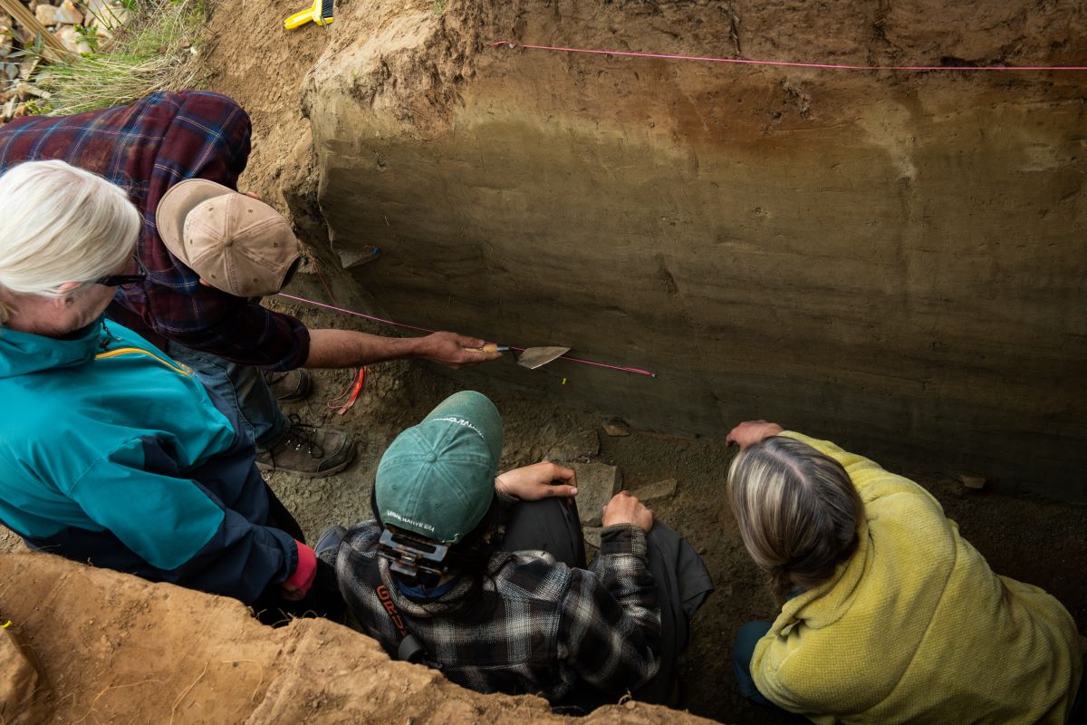 three students and a professor examine stratigraphic layers at an archaeology site