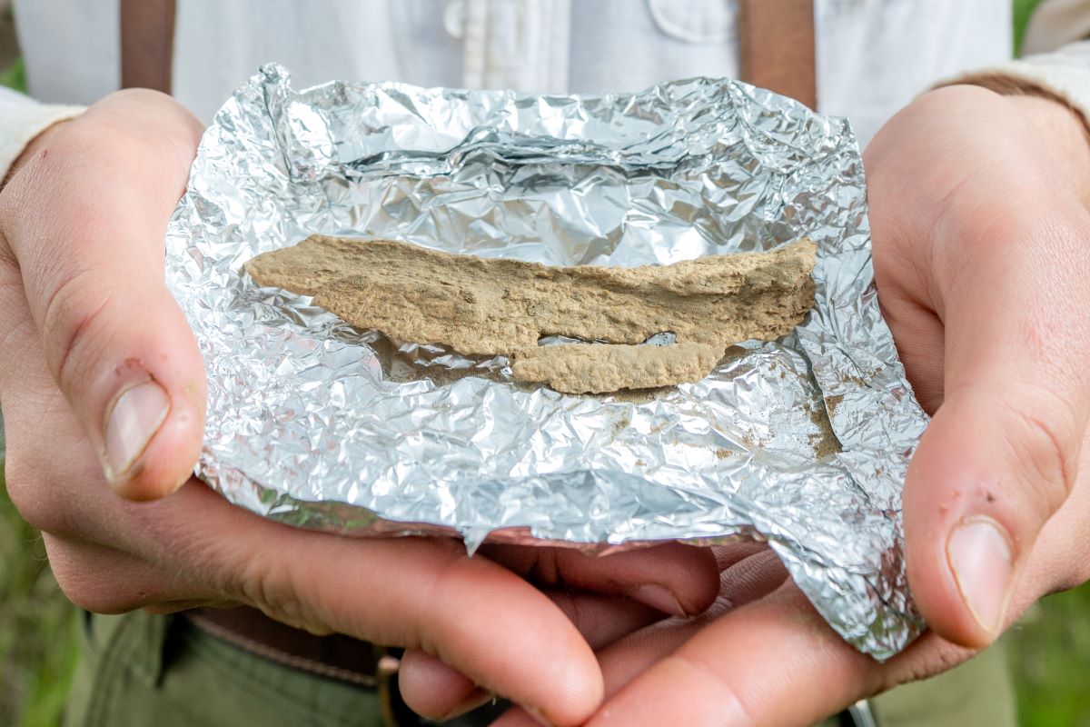 A student archaeologist holding a bone fragment wrapped in tin foil