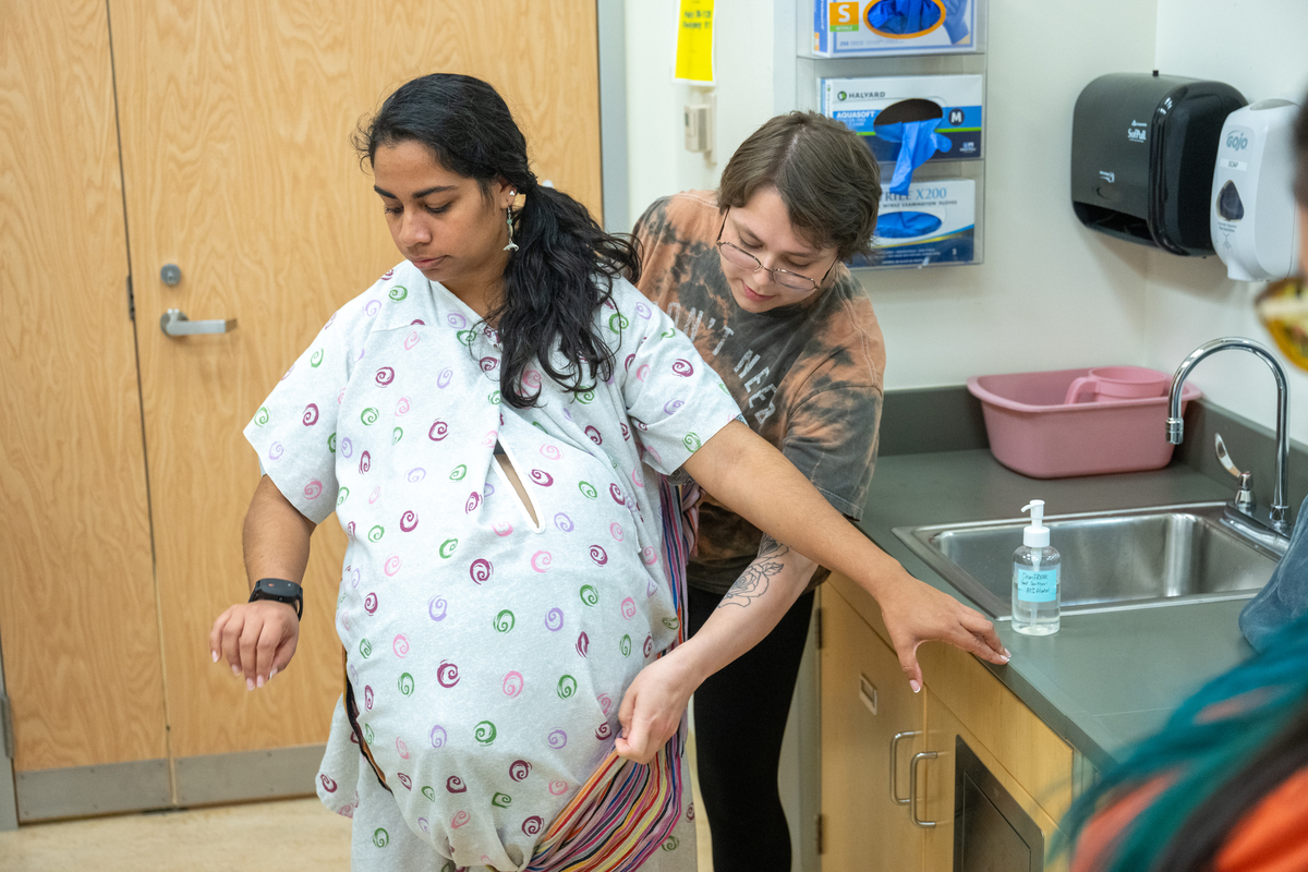 Student doula Alexanderia Hand helps Bethany Alvarez, portraying the expectant mother, as UAA College of Health Simulation Center uses a wearable Avbirth Childbirth Simulation Device for the first time to help train students in the Full Embrace Doula Program, which provides comprehensive education, mentorship, and capacity-building to expand access to culturally attuned birth support in Alaska.