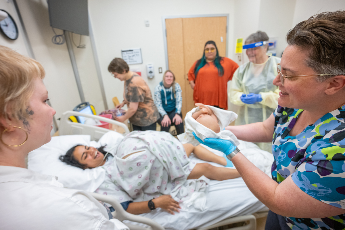 Simulation Center Director Sara Hannon presents the (simulated) newborn to Bethany Alvarez, portraying the expectant mother, as UAA College of Health Simulation Center uses a wearable Avbirth Childbirth Simulation Device for the first time to help train students in the Full Embrace Doula Program, which provides comprehensive education, mentorship, and capacity-building to expand access to culturally attuned birth support in Alaska.