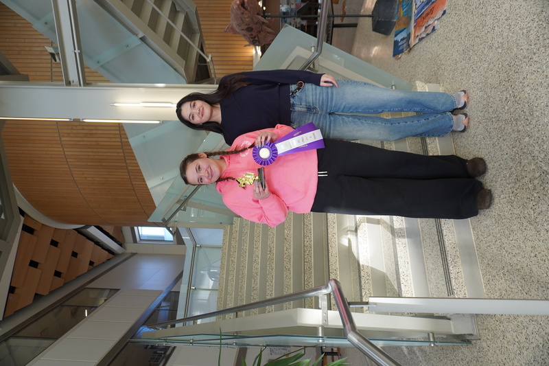 2026 Alaska Brain Bee winner Viola Voigt with championship ribbon and trophy, presented by 2025 Alaska Brain Bee winner Konnie Towner