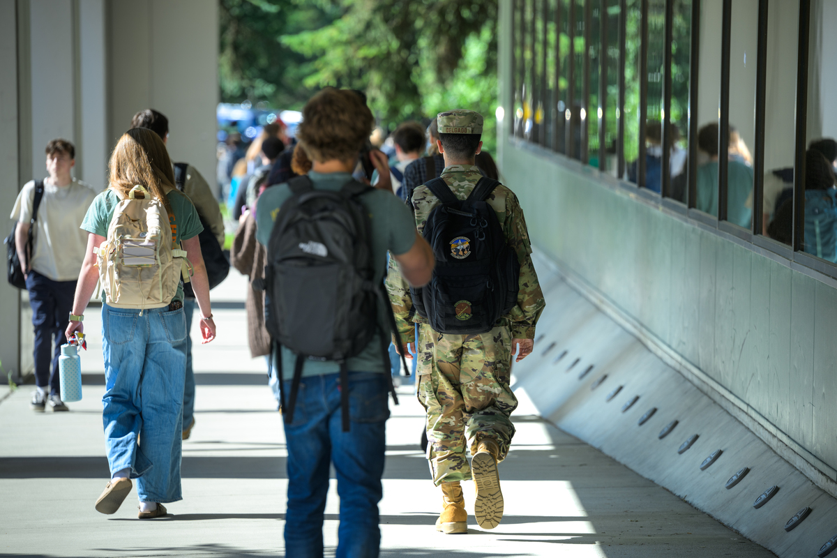 Students with backpacks, including one in military uniform, walk around campus