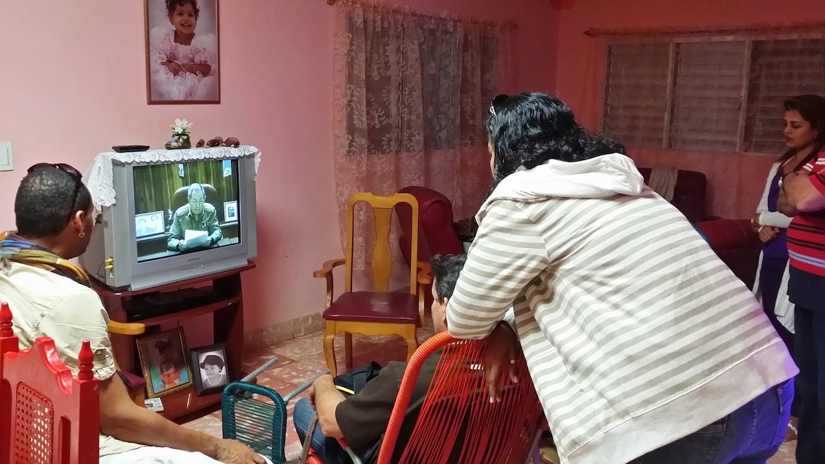 family watching TV announcement in living room with pink walls