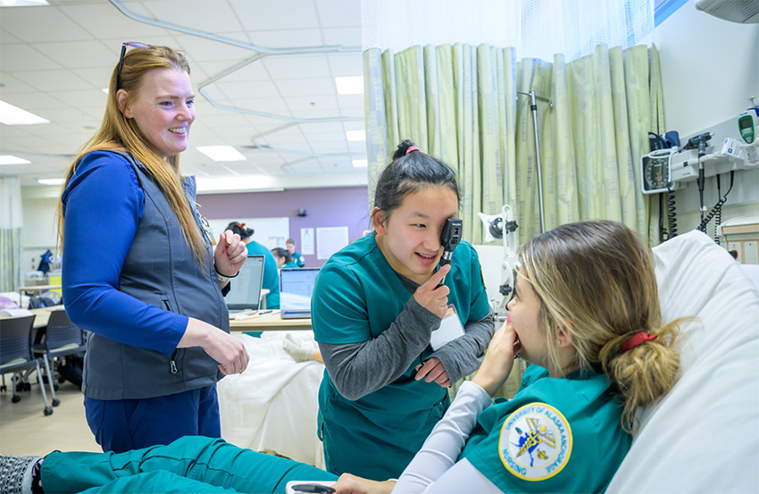 Jiaping Sliwinski and Emine Papraniku as nursing students learn exam procedures from Clinical Instructor Amber Garcia in the UAA Health Science Building simulation labs.
