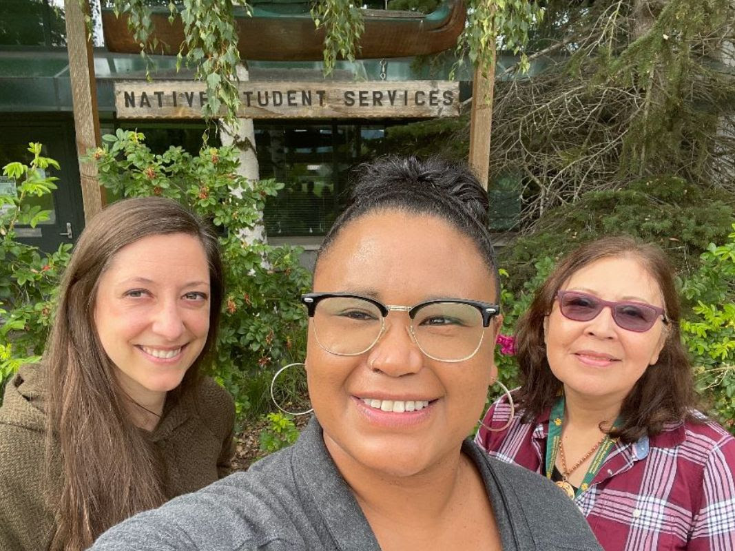 Three NSS staff outside in front of wooden carved Native Student Services sign